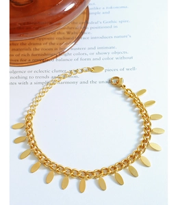 Detail of 18k gold plated Cuban chain bracelet with 14 smooth oval leaf charms on a book