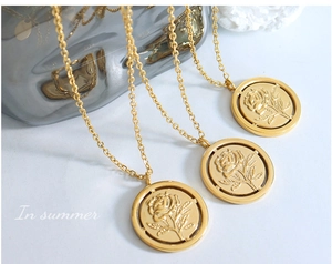 Détail d'un pendentif rose vintage doré avec relief floral et anneau évidé sur chaîne
