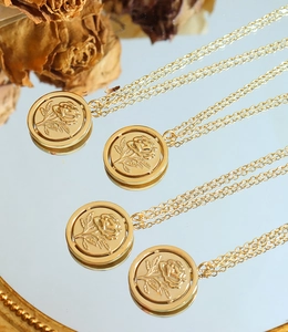 Vue détaillée de colliers pendentifs en relief de rose dorée sur une surface miroir