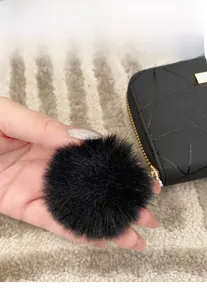 Dettaglio macro del ciondolo a sfera in lana nera su portafoglio trapuntato con zip