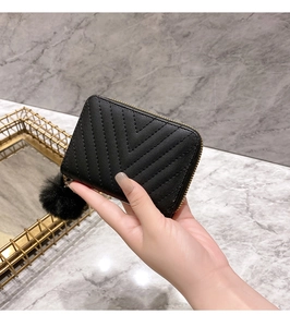 Detail of black V-quilted small wallet with faux fur pompom and gold zipper