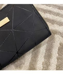 Dettaglio portafoglio nero con motivo geometrico, placca logo e cerniera dorata