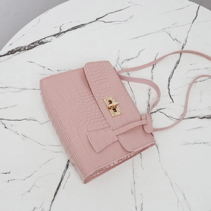 Sac bandoulière rose motif crocodile avec fermoir doré tournant sur fond de marbre blanc