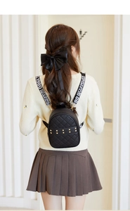 Détail de mini sac à dos noir matelassé avec clous dorés et bandoulière lettrée