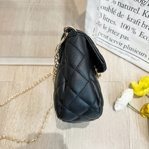 Close-up of black quilted small square bag with elegant gold chain and leather texture