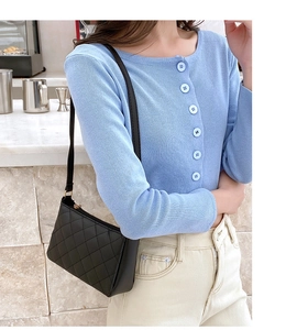 Close-up of black quilted underarm bag worn with a blue cardigan in an outdoor setting