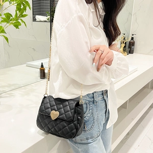 Detail of black quilted crossbody bag featuring a golden heart-shaped lock and chain strap