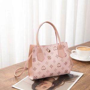 Close-up of pink monogram crossbody bag with heart pattern on a wooden surface