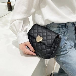 Detail of black quilted crossbody bag featuring a golden heart-shaped lock and chain strap
