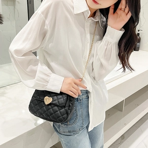 Detail of black quilted mini square bag with golden heart buckle and fine chain strap