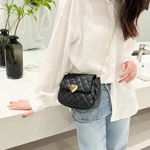 Detail of black quilted crossbody bag with gold heart buckle worn by model in white shirt