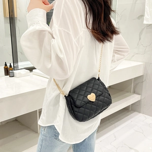 Detail of black quilted crossbody bag with golden heart lock worn over a white shirt