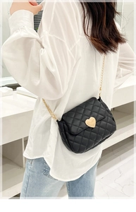 Detail of black quilted crossbody bag with gold heart clasp worn by model