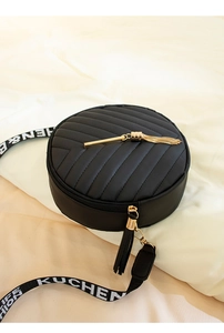 Close-up of black quilted round crossbody bag with golden tassel and woven strap