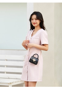 Detail of a mini black quilted jelly bag with gold lock and woven handle in outdoor setting