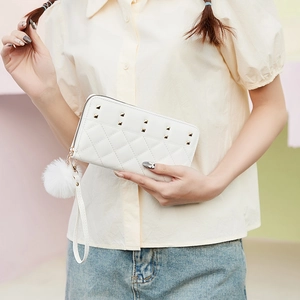White quilted long wallet with golden studs and fur pompom charm, held by model