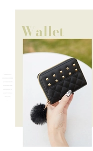 Close-up of black quilted wallet with golden square studs and a soft pompom charm