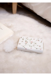 Close-up of white floral embroidery on women's wallet with soft plush pompom detail