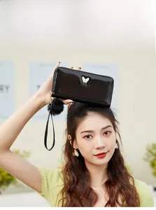 Close-up of black patent leather long wallet with butterfly buckle and fur pompom charm
