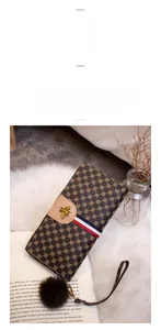 Detail of long monogram wallet with gold bee emblem, red striped ribbon and pompom