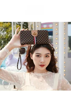 Long brown wallet with golden bee logo and colorful webbing held by a model