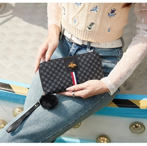 Detail of long black wallet featuring gold bee icon, tricolor ribbon and fuzzy pompom charm
