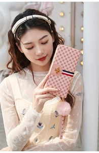 Pink long wallet detail with golden bee emblem, striped ribbon, and plush ball charm