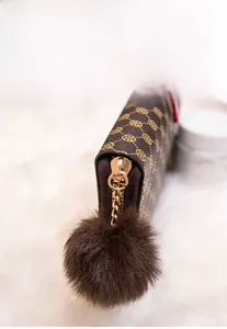 Detail of dark brown long wallet with golden clover print and fuzzy ball pendant