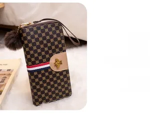 Detail of long brown leather wallet featuring colorful stripe, bee badge and fur ball zip
