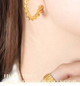 Detailed close-up of golden twist hoop earring and textured wide band ring on model
