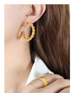 Detailed view of gold twisted C-shape earrings and textured wide band ring on a model