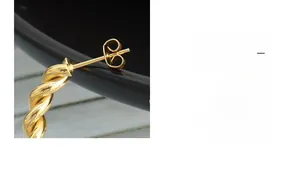 Close-up of bright gold twisted C-shape stud earring with polished finish