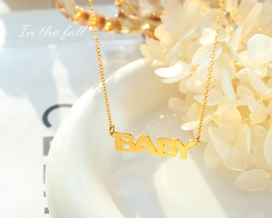 Dettaglio di una collana dorata con ciondolo a lettere baby su una ciotola di ceramica