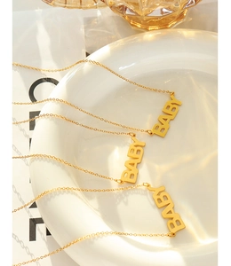 Dettaglio della collana dorata in acciaio inossidabile con ciondolo Baby su un piatto ceramico