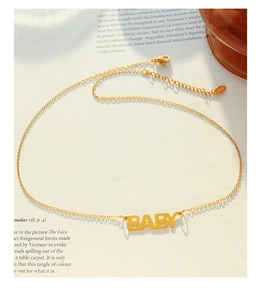 Dettaglio della collana in oro 18K con ciondolo a lettere BABY su una pagina di libro