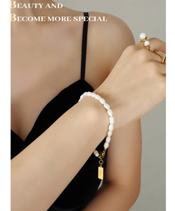 Dettaglio del bracciale di perle con ciondolo LOVE e anelli d'oro su una modella