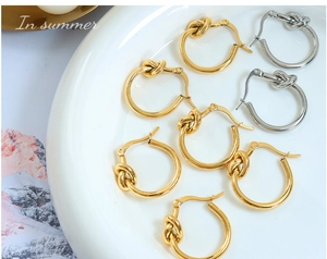 Détail de boucles d'oreilles créoles avec nœud en or et argent sur un plateau en céramique