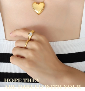 Primer plano de un collar con colgante de corazón dorado grande y anillos texturizados