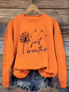 Détail du sweat orange Just Breathe avec motif pissenlit sur un cintre en bois