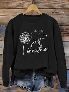 Détail de l'imprimé pissenlit Just Breathe sur un sweat-shirt noir suspendu sur bois