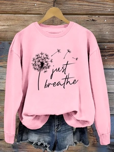 Détail du sweat rose avec imprimé pissenlit et texte Just Breathe sur un cintre en bois