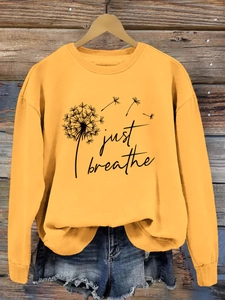 Détail d'un sweat-shirt jaune avec imprimé pissenlit Just Breathe sur un cintre