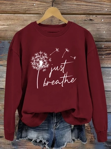 Détail d'un sweat bordeaux 'Just Breathe' avec imprimé pissenlit blanc sur cintre en bois