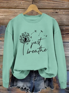 Gros plan du sweat pissenlit vert menthe avec texte Just Breathe sur fond bois