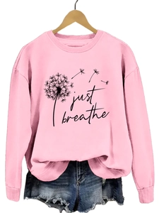 Détail du sweat rose avec imprimé pissenlit et texte just breathe sur cintre en bois