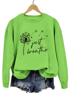 Détail du sweat vert Just Breathe avec imprimé pissenlit sur un cintre en bois