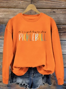 Detail of orange pickleball sweatshirt with ribbed neckline on a wooden hanger background