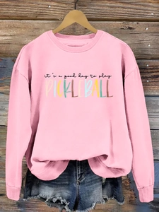 Detailed view of pink pickleball graphic sweatshirt on a wooden hanger with denim shorts