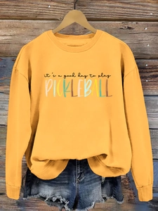 Detail of a mustard yellow sweatshirt with retro Pickleball print on a wooden background