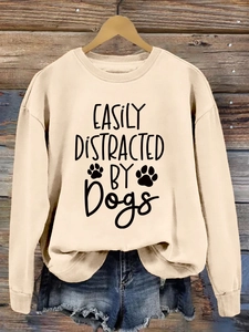 Close-up of 'Easily Distracted by Dogs' print on a beige crewneck sweatshirt on wood wall